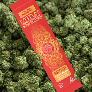 Red pre-roll packaging with orange designs on a bed of green cannabis buds.