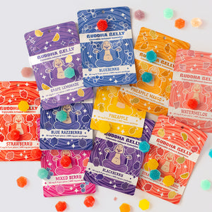 Colorful packaging of Buddha Belly cannabis gummy products on a white background with candy accents.