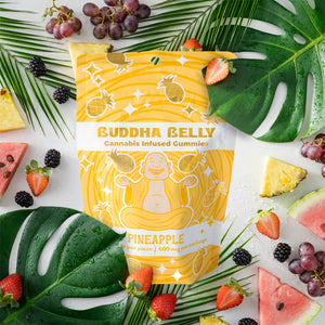 Buddha Belly cannabis-infused gummies packaging with pineapple flavor on a colorful background with fruits and leaves.