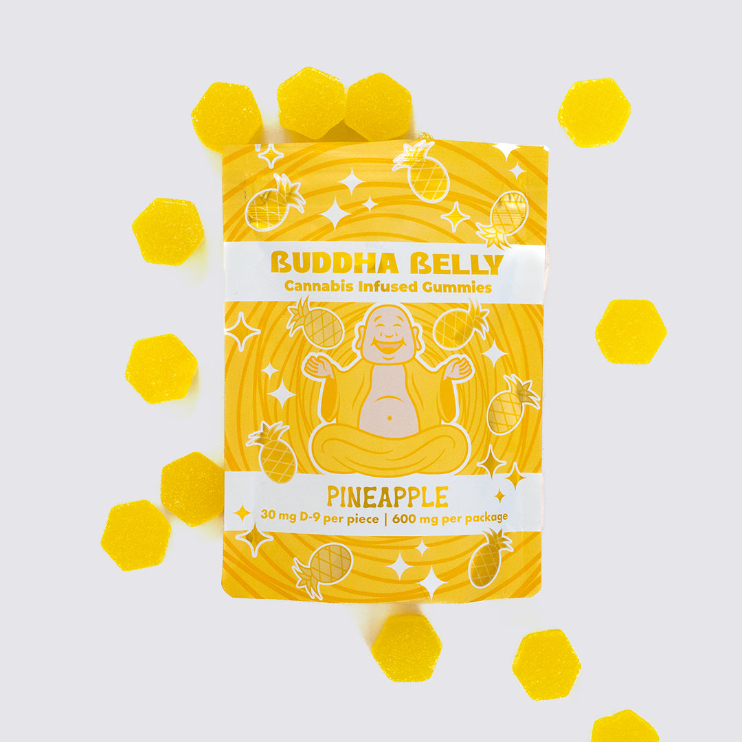 Packaging of Buddha Belly Pineapple flavored gummies on a light gray background with scattered pineapple slices.